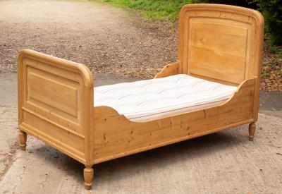 A pine single bed with mattress, rounded