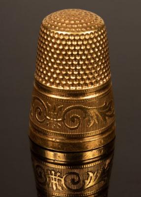 A gold thimble with engraved borders,