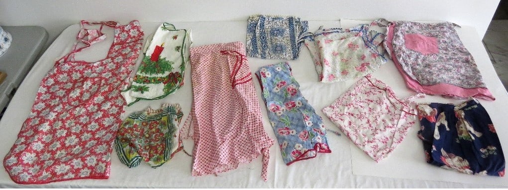 A TABLE LOT OF 10 VINTAGE APRONS OF